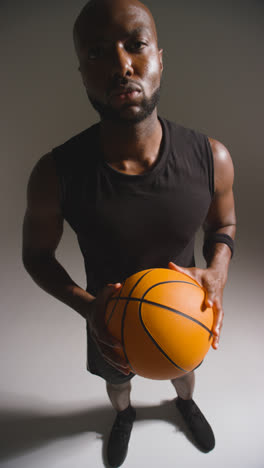 Vertical-Video-Vertical-Video-Portrait-Studio-Shot-Looking-Down-On-Male-Basketball-Player-Dribbling-And-Bouncing-Ball-Against-White-Background